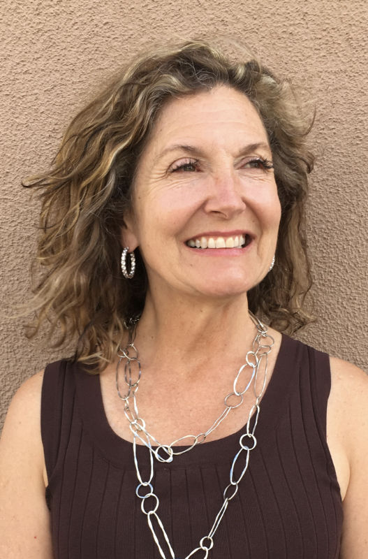 Portrait of a smiling woman with curly hair, wearing a silver chain necklace, set against a plain background, exuding a warm and professional demeanor.