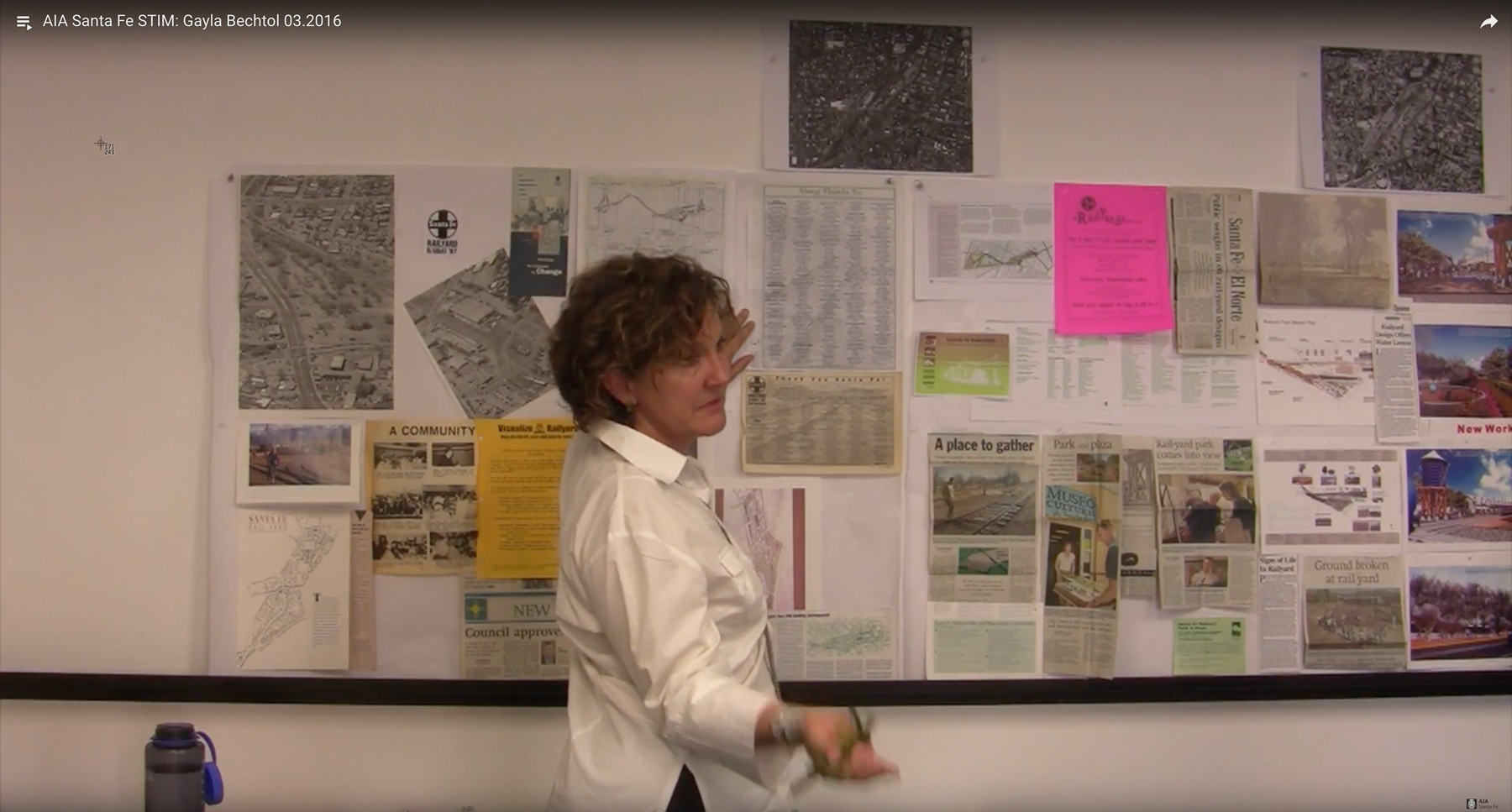 Photo of architect Gayla Bechtol standing in front of a wall covered with various planning documents, aerial photos, and newspaper articles, discussing the Santa Fe Railyard project in March 2016.