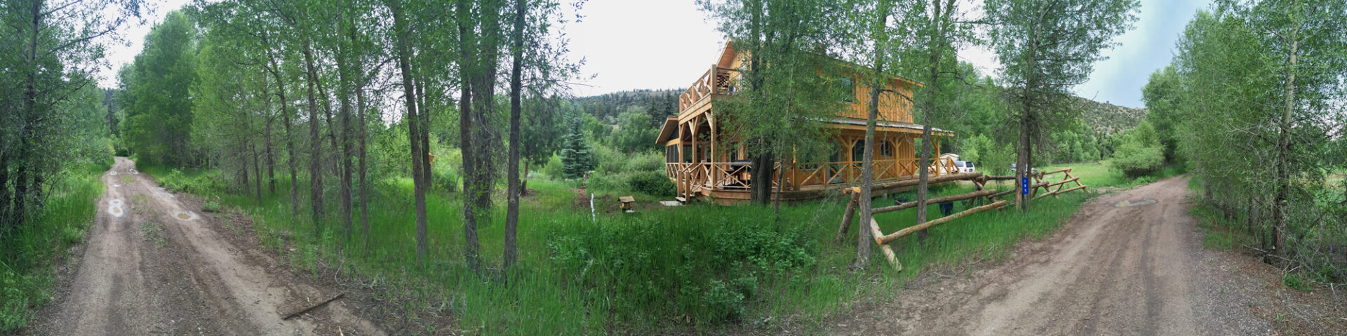 Panoramic view of architect-designed cabin in lush forest, showcasing sustainable residential architecture with a screened porch and natural surroundings.